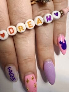 Dream bracelet on hand with pink and purple nails that say dream and have a mickey mouse outline.